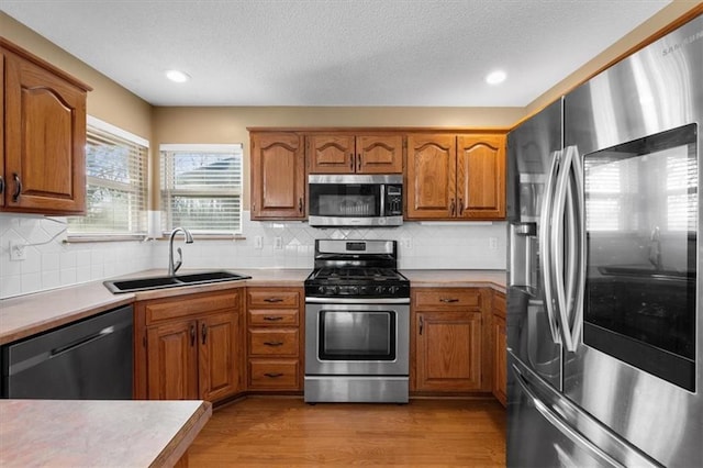 kitchen featuring light wood finished floors, appliances with stainless steel finishes, brown cabinets, light countertops, and a sink