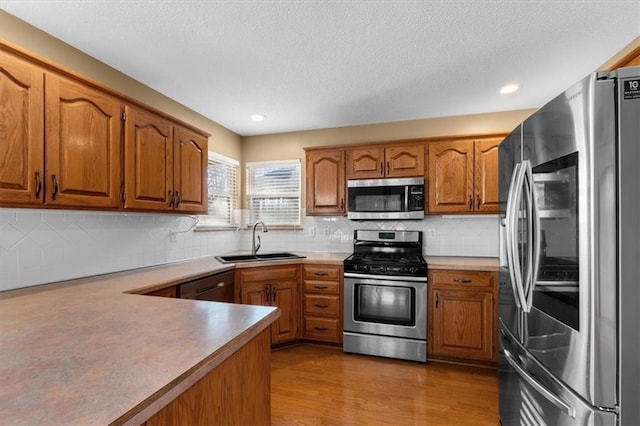 kitchen featuring brown cabinets, wood finished floors, a sink, stainless steel appliances, and backsplash