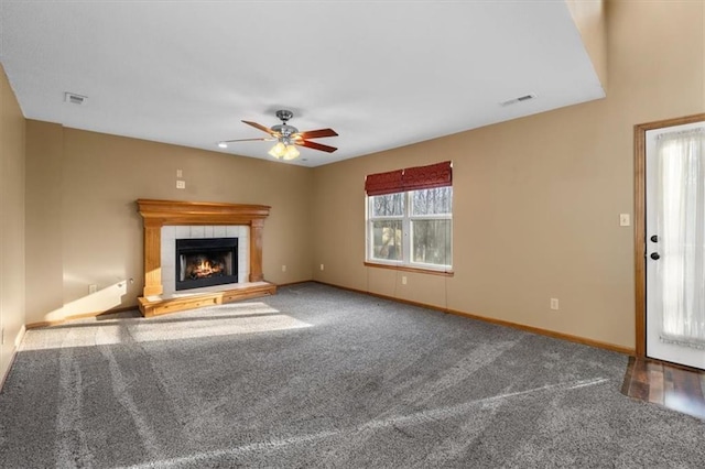 unfurnished living room with baseboards, visible vents, a ceiling fan, a tile fireplace, and carpet flooring