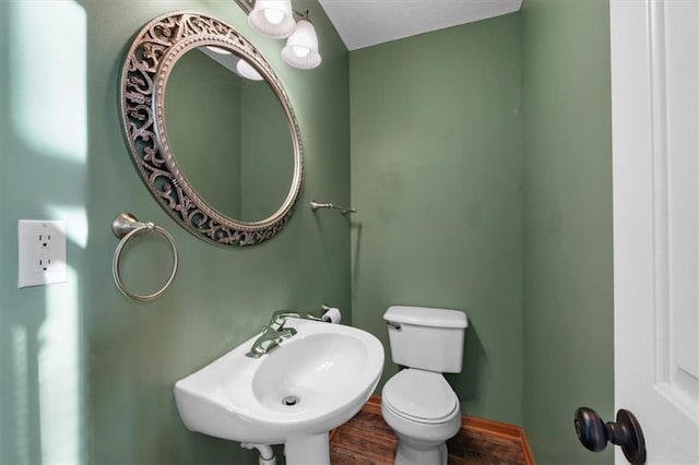 half bath with toilet, a sink, and wood finished floors