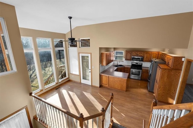 kitchen with lofted ceiling, appliances with stainless steel finishes, brown cabinets, wood finished floors, and a sink