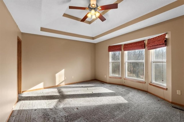 carpeted spare room with a ceiling fan, a tray ceiling, visible vents, and baseboards