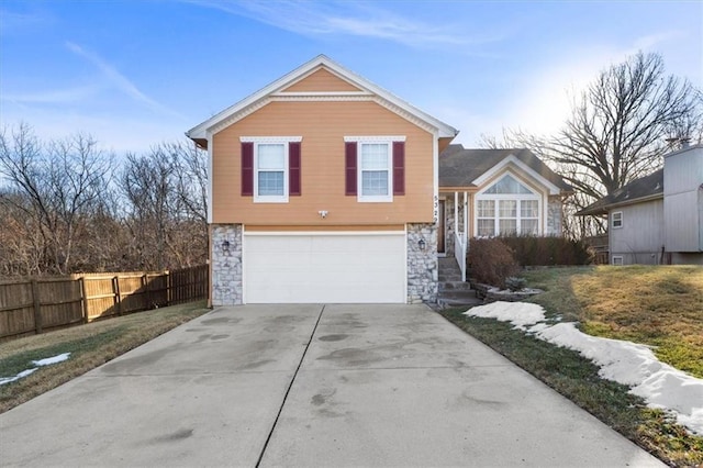 tri-level home featuring a garage, stone siding, fence, and driveway