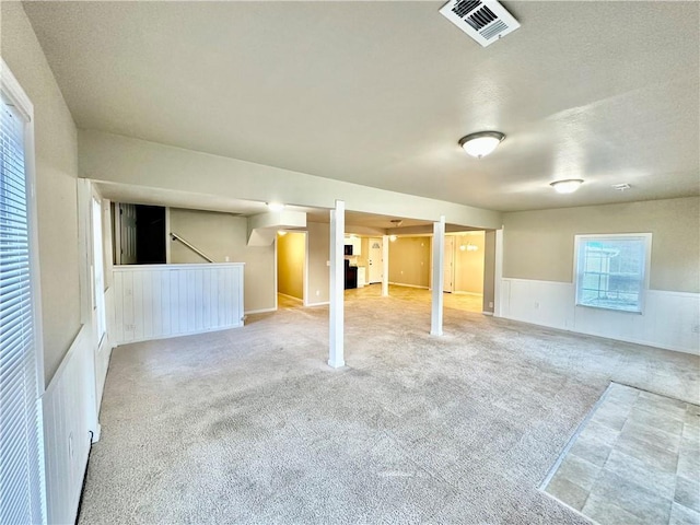 basement with light carpet, a wainscoted wall, a textured ceiling, and visible vents