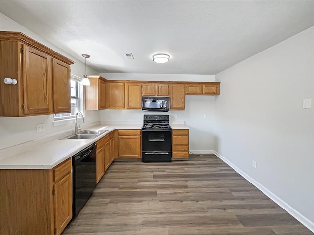 kitchen with a sink, light countertops, black appliances, brown cabinetry, and decorative light fixtures