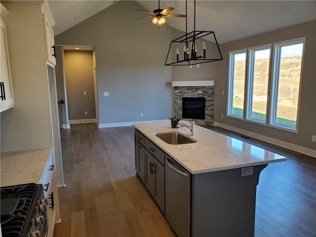 kitchen with stainless steel appliances, wood finished floors, open floor plan, a sink, and light stone countertops