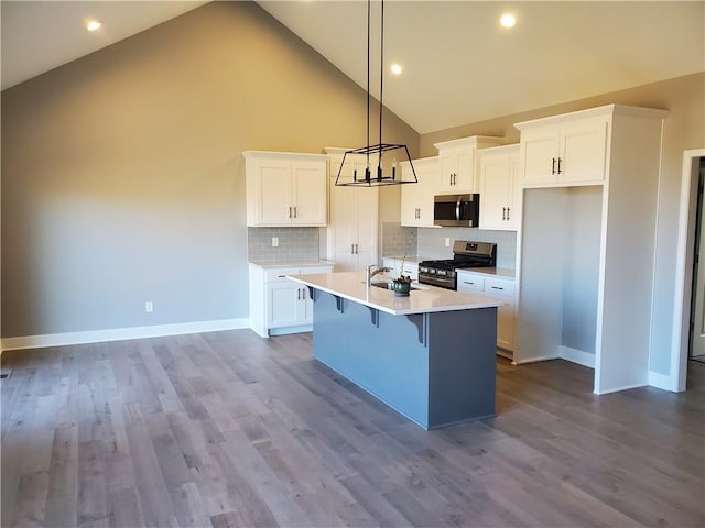 kitchen with white cabinetry, light countertops, appliances with stainless steel finishes, a kitchen bar, and a center island with sink