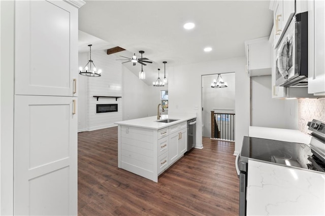 kitchen featuring a large fireplace, vaulted ceiling, stainless steel appliances, white cabinetry, and a sink