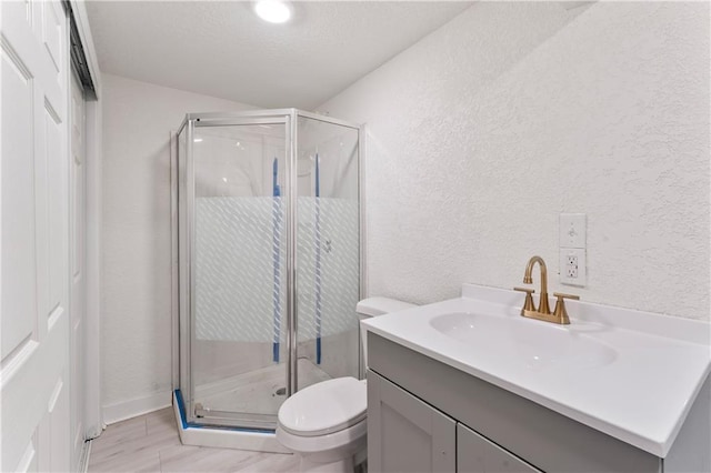 bathroom featuring a textured wall, a shower stall, toilet, and vanity