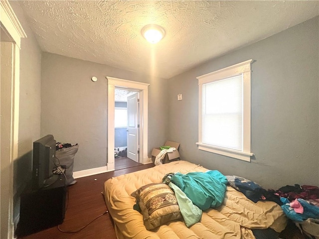 bedroom featuring multiple windows, baseboards, dark wood finished floors, and a textured ceiling