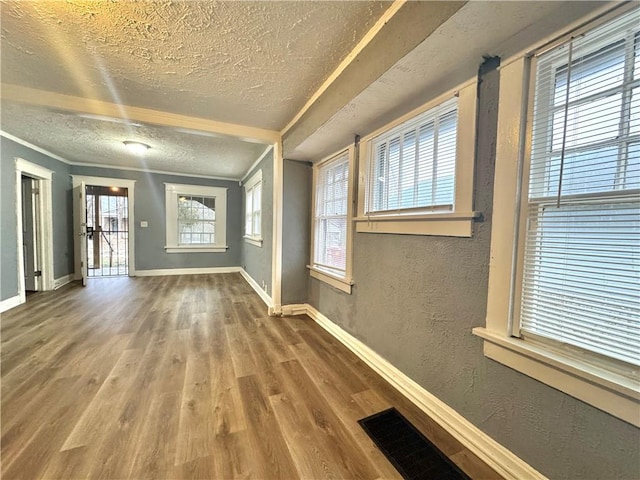 interior space featuring baseboards, visible vents, a textured wall, wood finished floors, and a textured ceiling