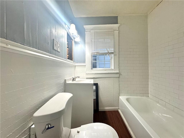 bathroom with toilet, wood finished floors, vanity, tile walls, and a bath