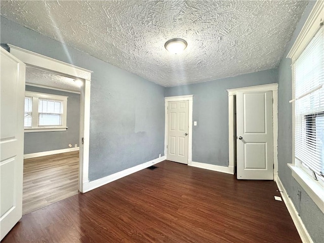 unfurnished room with dark wood-style flooring, a textured ceiling, and baseboards