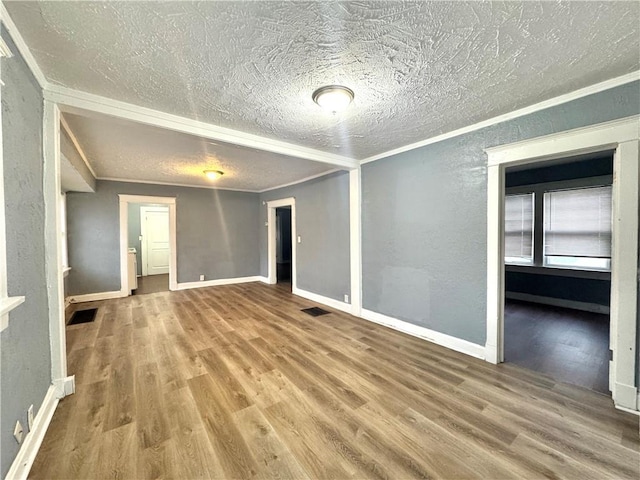 empty room with ornamental molding, wood finished floors, visible vents, and baseboards