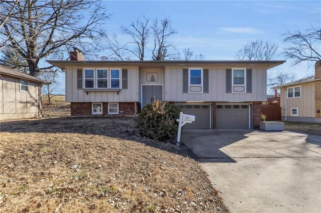 split foyer home with concrete driveway, brick siding, board and batten siding, and a chimney