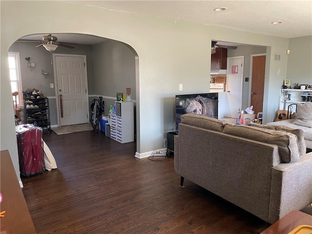 living room with baseboards, arched walkways, dark wood-type flooring, and a ceiling fan