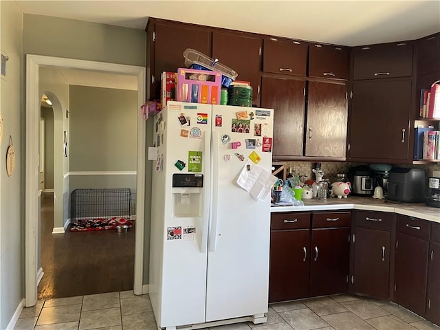 kitchen with light tile patterned floors, arched walkways, light countertops, dark brown cabinetry, and white refrigerator with ice dispenser