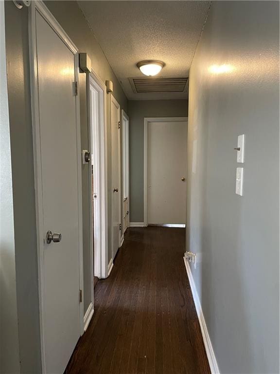 hallway featuring visible vents, dark wood-type flooring, a textured ceiling, and baseboards