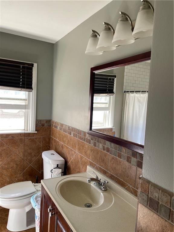 full bath featuring a wealth of natural light, toilet, tile walls, and vanity