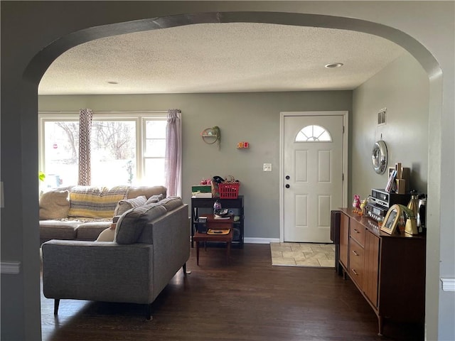 entrance foyer featuring baseboards, arched walkways, a textured ceiling, and dark wood-style floors