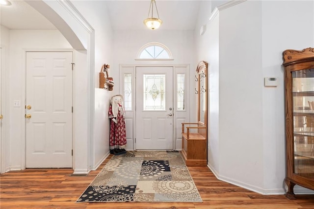 entrance foyer with arched walkways, baseboards, and wood finished floors