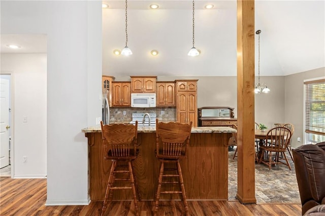 kitchen featuring a breakfast bar, white appliances, vaulted ceiling, and a peninsula