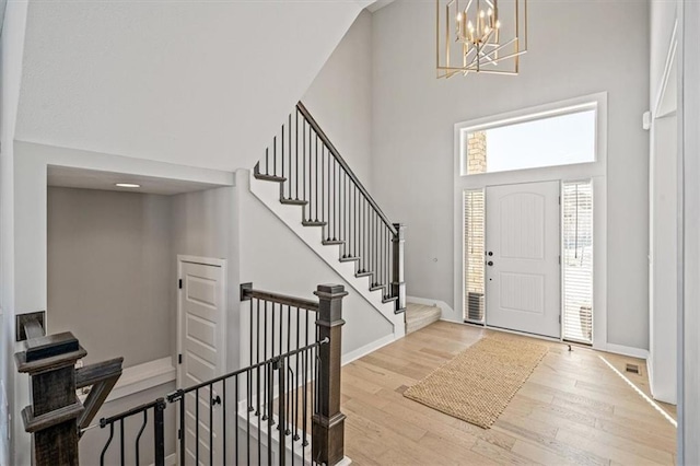 foyer entrance featuring light wood finished floors, baseboards, an inviting chandelier, stairs, and a high ceiling