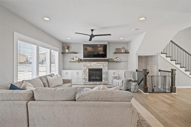 living room with ceiling fan, a stone fireplace, light wood finished floors, and recessed lighting