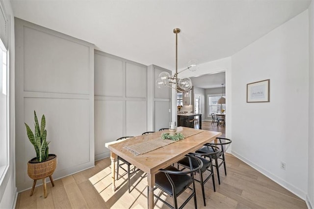 dining area featuring light wood-style flooring, baseboards, a decorative wall, and a notable chandelier