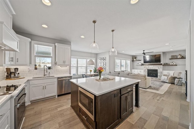 kitchen with appliances with stainless steel finishes, white cabinetry, a sink, a stone fireplace, and dark brown cabinets