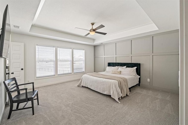 bedroom featuring a tray ceiling, light colored carpet, a decorative wall, and baseboards