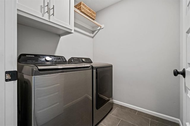 clothes washing area featuring cabinet space, washing machine and dryer, baseboards, and dark tile patterned floors