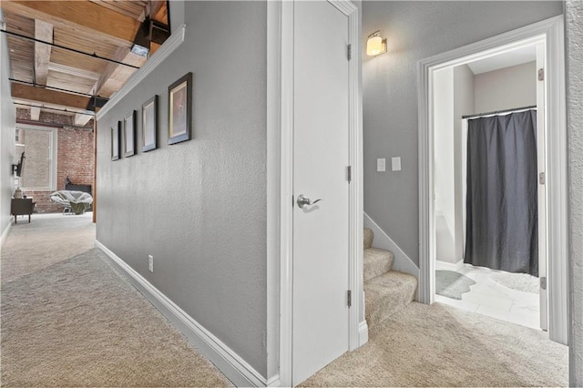 corridor with a textured wall, stairway, and light colored carpet