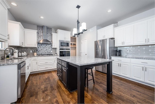 kitchen with a center island, appliances with stainless steel finishes, white cabinetry, a sink, and wall chimney range hood