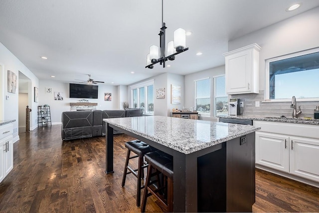 kitchen featuring a kitchen island, open floor plan, decorative light fixtures, white cabinetry, and a sink