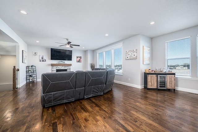 living area with ceiling fan, a stone fireplace, recessed lighting, dark wood-style flooring, and baseboards