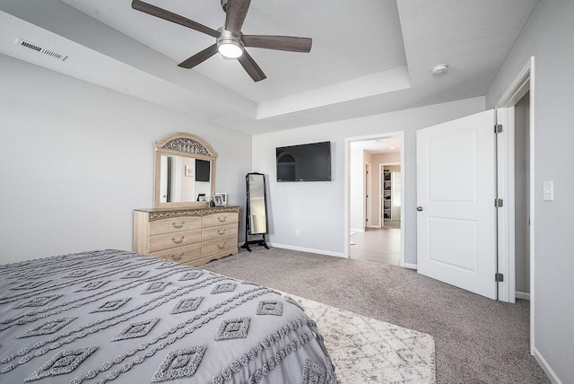 bedroom with a raised ceiling, visible vents, light carpet, ceiling fan, and baseboards