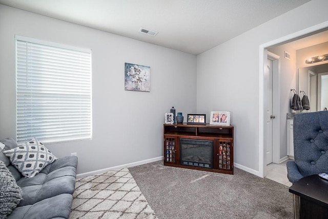 interior space featuring light carpet, a glass covered fireplace, visible vents, and baseboards