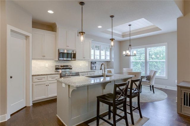 kitchen featuring stainless steel appliances, a sink, white cabinetry, light stone countertops, and pendant lighting