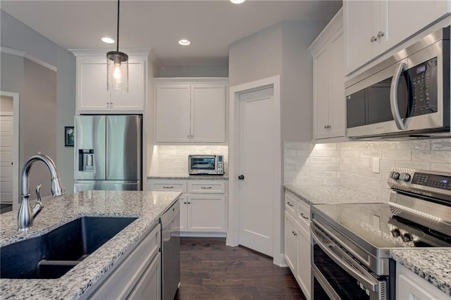 kitchen featuring white cabinets, appliances with stainless steel finishes, hanging light fixtures, light stone countertops, and a sink