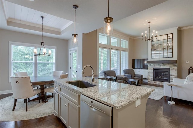 kitchen featuring light stone counters, a sink, dishwasher, a raised ceiling, and a center island with sink