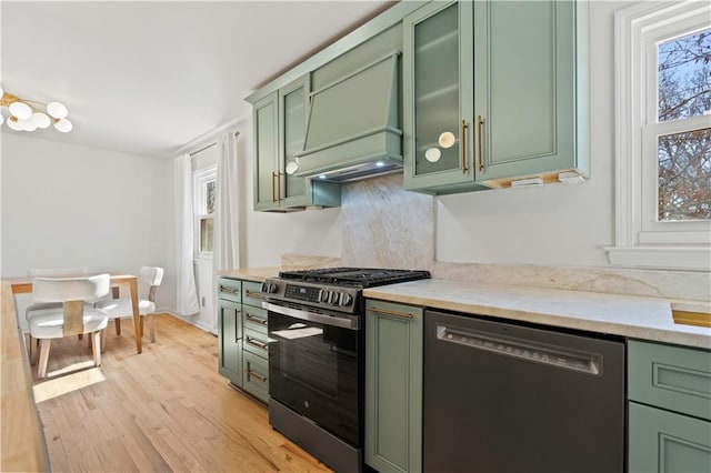 kitchen featuring stainless steel range with gas cooktop, black dishwasher, light wood finished floors, green cabinetry, and premium range hood