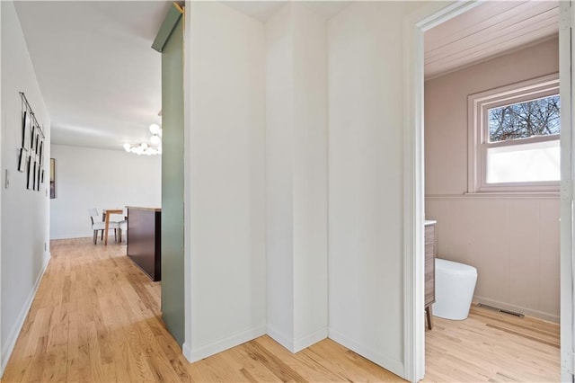 hallway featuring baseboards, an inviting chandelier, visible vents, and light wood-style floors