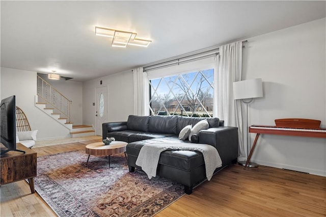 living area featuring light wood-style flooring, stairs, and baseboards