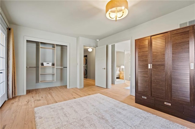 unfurnished bedroom featuring wood finished floors, visible vents, baseboards, stacked washer / drying machine, and a closet