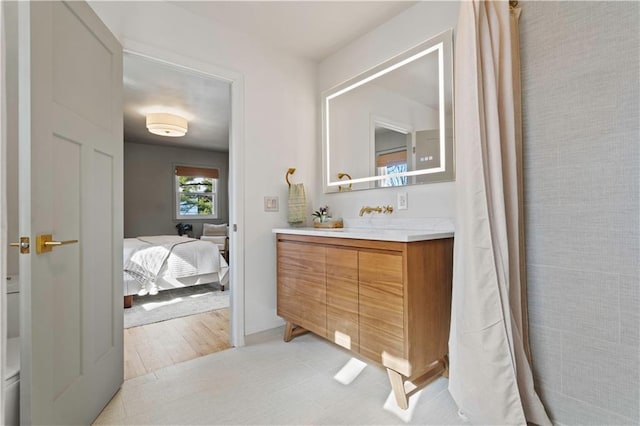 ensuite bathroom with connected bathroom, wood finished floors, and vanity