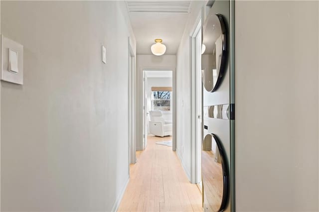 hall with stacked washing maching and dryer, baseboards, and light wood finished floors