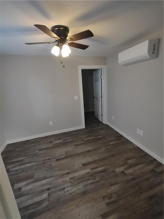 spare room featuring a ceiling fan, dark wood-style flooring, a wall unit AC, and baseboards