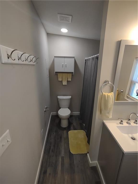 bathroom featuring visible vents, toilet, vanity, wood finished floors, and baseboards