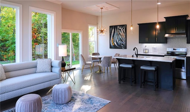 kitchen with a center island with sink, electric stove, open floor plan, hanging light fixtures, and light countertops